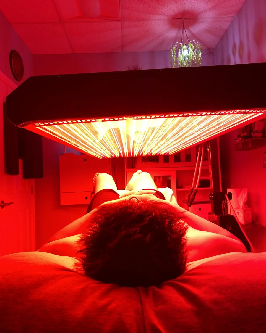 Client resting under the full-body red light therapy panel in the Escondido treatment room